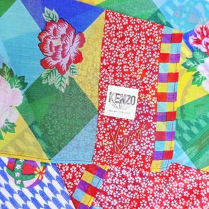 May include: A Kenzo handkerchief featuring a vibrant patchwork design of blue, yellow, and green diamonds, red floral patterns, and small white blossoms. A white square label with the text KENZO is stitched on, with the brand name embroidered below.