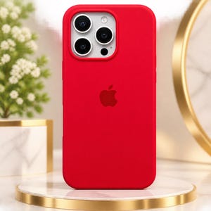 May include: A vibrant red silicone phone case designed for an iPhone Pro model, featuring a prominent Apple logo centred on the back. The case includes a precise cutout for the triple-lens camera system, flash, and microphone array on the top left.