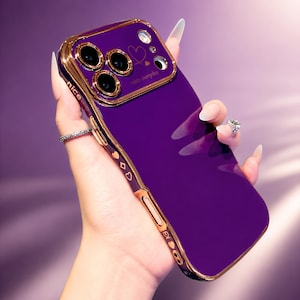 Op de afbeelding: Een dieppaarse smartphonehoes met een metallic goudkleurig frame en rand rond de cameralenzen. De achterkant toont een kleine gouden hartomtrek, een gevuld gouden hart en de tekst "nice everyday". De zijkant is voorzien van kleine hartjes.
