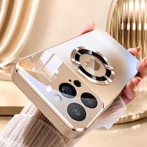 Puede incluir: Una funda de smartphone en tono dorado con un anillo de carga magnético circular en la parte posterior, una abertura para triple cámara con panel reflectante y el texto "AUTOFOCUS" impreso cerca del módulo de la cámara. Acabado metálico.
