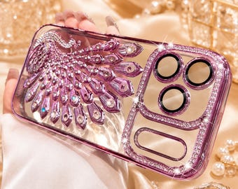 Puede incluir: Una funda de teléfono transparente con un diseño de pavo real morado adornado con pedrería. El área de la lente de la cámara está enmarcada por un borde de cristales brillantes, y los bordes tienen un acabado en tono morado metálico.