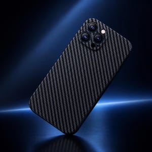 Könnte beinhalten: Ein Smartphone mit einer schwarzen und dunkelgrauen Carbonfaser-Texturfolie auf der Rückseite. Das Gerät verfügt über ein dreifaches Kameraobjektiv in dreieckiger Anordnung sowie einen kreisförmigen Blitz auf der rechten Seite des Moduls.