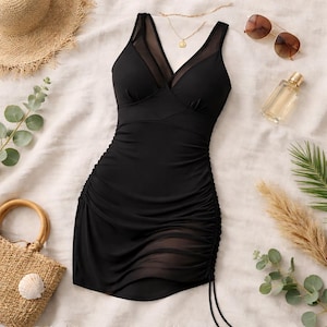 Puede incluir: Un vestido de baño negro con escote en V y detalles de malla. El vestido presenta fruncidos en los laterales y un cordón. Accesorios: sombrero de paja, gafas de sol, collar dorado, frasco de perfume y bolso tejido.