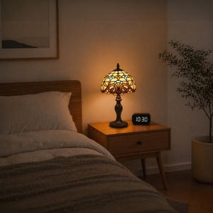 May include: A stained glass table lamp with a bronze base sits on a wooden nightstand. The lamp has a colorful, patterned shade. A digital clock displaying "10:30" is next to the lamp. The bedroom has a bed with a wooden headboard.