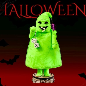 May include: A bright green plush figure of Oogie Boogie with a stitched mouth, black eyes, and a worm protruding from its mouth. The figure holds two white dice with black dots and has a small purple spider attached to its head, standing on a base.