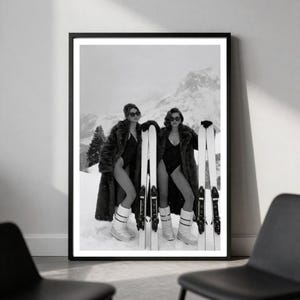 May include: A black and white framed wall art print depicting two individuals in dark swimsuits and long fur coats, wearing sunglasses and white snow boots, standing in a snowy mountain landscape while holding tall white skis in their hands.