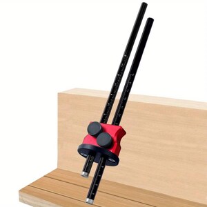 May include: A red and black woodworking marking gauge with two black rods featuring measurement markings. The gauge is positioned against a wooden surface, showcasing its use in carpentry and woodworking projects.