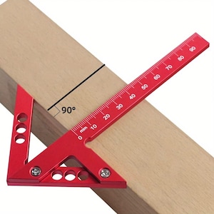 May include: A red aluminium speed square on a wooden plank, showing a 90-degree angle. The square has measurements in millimetres, used for carpentry and construction projects.