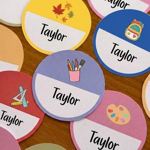 May include: A collection of circular paper labels in various colours including yellow, blue, purple, pink, and red. Each label features a white semi-circle section with the name Taylor printed in black text and a small colourful icon above the name.