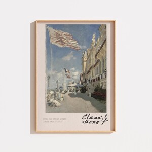 May include: A framed art print featuring Claude Monet's painting of the Hotel des Roches Noires. The scene depicts a building facade, a large flag waving in the blue sky, and figures on a walkway. The text reads Hotel des Roches Noires, Claude Monet 1870.