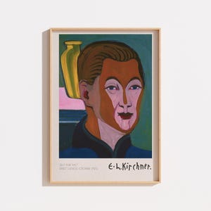 May include: A framed art print of a self-portrait by Ernst Ludwig Kirchner. The painting features a person with a brown face, pink highlights, and dark hair, wearing a blue garment. A yellow vase sits in the background. Text reads E. L. Kirchner.