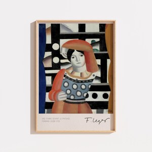 Peut inclure: Une impression d'art encadrée représentant une figure avec un couvre-chef rouge, un corsage bleu à pois blancs et des manches orange. L'arrière-plan présente une grille noire et blanche. Le texte en bas indique UNE FEMME DEVANT LE PAYSAGE FERNAND LEGER 1921 et F. Leger.