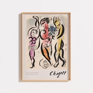 Peut inclure: Une impression d'art encadrée intitulée Les Trois Acrobates de Marc Chagall, représentant trois personnages stylisés aux tons violets, rouges et jaunes avec des contours noirs. L'affiche inclut le texte Les Trois Acrobates, Marc Chagall 1975, et Chagall.