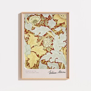 Peut inclure: Une impression d'art encadrée présentant un motif floral de William Morris avec des feuilles et des fleurs jaune pâle et vert clair sur un fond rouge profond. La marge inférieure inclut le texte Bachelor's Button, William Morris, 1892, et une signature.