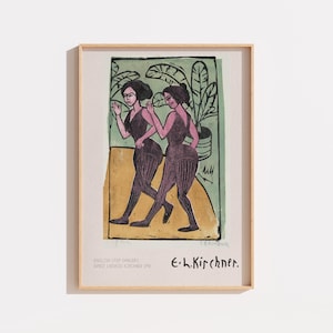 May include: A framed art print featuring the work English Step Dancers by Ernst Ludwig Kirchner. The image depicts two figures in dark purple leotards against a green background with potted plants, set on a tan ground. Text includes the title and artist name.