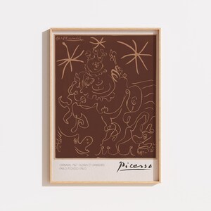 May include: A framed art print featuring a dark brown background with light beige line art depicting a clown and dancers. The text reads Carnival 1967 Clown et Danseurs Pablo Picasso 1967 and Picasso. The print is enclosed in a light wood frame.