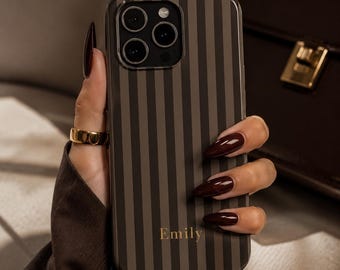 May include: A smartphone case featuring a vertical striped pattern in alternating shades of dark brown and light brown. The name Emily is printed in a gold serif font near the bottom center of the case. The case has a cutout for a triple camera system.