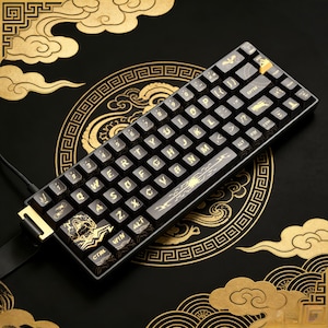 May include: A black and gold mechanical keyboard with a 60% layout. The keycaps are black with gold lettering and decorative designs. The keyboard has a gold-coloured frame and is connected by a black cable. The background is black with gold cloud and geometric patterns.