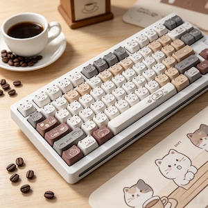 May include: A white mechanical keyboard with cat-shaped keycaps in various colors, including white, gray, and brown. The keyboard has a coffee-themed design, with coffee beans and a cup of coffee visible in the background. A matching mousepad is also present.