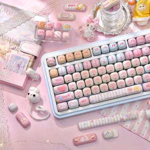 May include: A pastel-colored keyboard with custom keycaps featuring cute animal designs. The keyboard has a light blue frame and a variety of decorative accessories, including additional keycaps and a wrist rest. The overall aesthetic is soft and feminine.