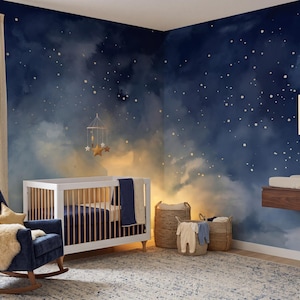 Op de afbeelding: Een kinderkamer met een hemels thema. De kamer heeft een witte wieg, een marineblauwe schommelstoel en een tapijt met een blauw patroon. De muren zijn beschilderd met een nachthemelontwerp en een mobiel met stervormige ornamenten hangt boven de wieg.