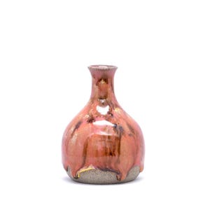 Puede incluir: Un pequeño jarrón de cerámica hecho a mano con cuerpo redondeado y cuello estrecho. El jarrón presenta un esmalte brillante de color marrón rojizo con vetas más oscuras y una base texturizada sin esmaltar. El jarrón mide unos 13 cm de altura.