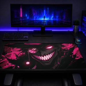 May include: A rectangular desk mat featuring a dark, high-contrast graphic of a grinning character with glowing pink eyes, a monocle, and sharp teeth. The design uses a black and vibrant pink color palette, covering the entire surface of the mat.