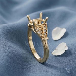 May include: A yellow gold ring setting featuring a four-prong head designed to hold a center stone. The shoulders of the band are accented with two vertical rows of small, round, clear stones set within a decorative metal frame.