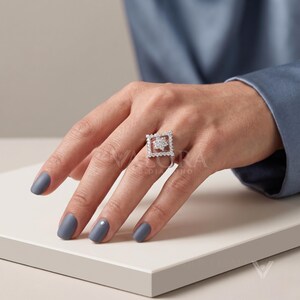 Lifestyle finger shot displays the delicate geometry of a women's ring worn elegantly on hand model. This vintage inspired moissanite statement piece fits true to size for comfortable everyday styling. Features a custom split shank 14k gold band that frames a sparkling diamond cut open halo perfectly. Captures true brilliance and elite conversion appeal, offering trendy jewelry accents for any buyer.