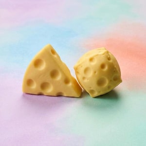 May include: Two pieces of yellow cheese with holes, one triangular and one round, are displayed against a colourful backdrop. The cheese has a smooth texture and a light yellow colour.