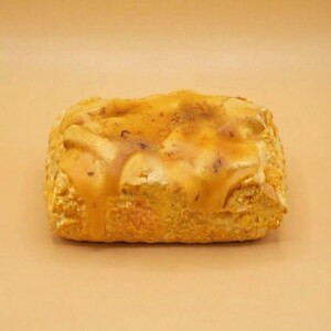 Pode incluir: Um pastel retangular assado com uma crosta texturizada castanho-dourada, coberto com um glacê espesso, brilhante e de cor âmbar que escorre pelas laterais, criando uma camada lisa e translúcida sobre a superfície porosa da massa.