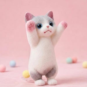 Könnte beinhalten: Eine kleine, beflockte Katzenfigur, die auf den Hinterbeinen steht und die Vorderpfoten hebt. Die Katze hat einen weißen Körper, graue Flecken an Kopf und Beinen, rosa gefärbte Ohren und Pfoten sowie große, dunkelblaue Augen und einen Mund.