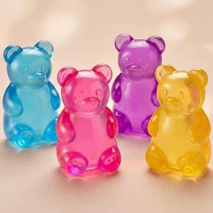 May include: Four translucent gummy bear sweets in blue, pink, purple, and yellow. The bears are in a playful, upright pose, with visible details. The image has soft lighting. Each bear is approximately 5 cm tall.