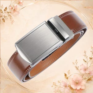 May include: A brown leather belt featuring a rectangular, brushed silver-tone metal buckle with a sliding ratchet mechanism. The belt strap has visible stitching along the edges and a smooth finish, presented in a coiled position.