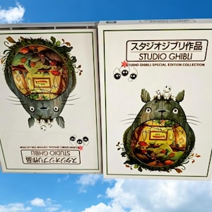 Pode incluir: Duas caixas da cole&ccedil;&atilde;o de edi&ccedil;&atilde;o especial Studio Ghibli. Cada caixa apresenta um personagem Totoro cinza com uma cena interior detalhada. O texto "STUDIO GHIBLI" e caracteres japoneses s&atilde;o vis&iacute;veis.