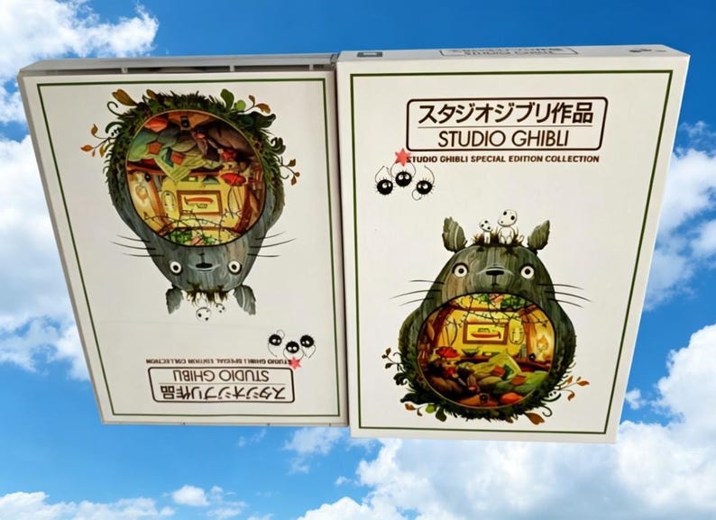Pode incluir: Duas caixas da cole&ccedil;&atilde;o de edi&ccedil;&atilde;o especial Studio Ghibli. Cada caixa apresenta um personagem Totoro cinza com uma cena interior detalhada. O texto "STUDIO GHIBLI" e caracteres japoneses s&atilde;o vis&iacute;veis.