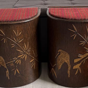 May include: A pair of dark brown wooden stools with red upholstered seats. Each stool has a carved bird and bamboo design. The stools are cylindrical in shape and are likely made of hardwood.