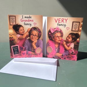 May include: Two greeting cards featuring a child applying makeup to a grandmother. The left card reads I made Grandma fancy. The right card reads VERY fancy. Both cards show a child and grandmother with pink accents, makeup brushes, and mirrors.