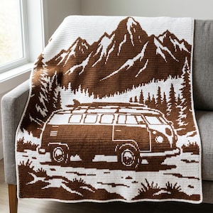 Pode incluir: Uma manta de crochê retangular com um design bicolor em marrom e branco. O padrão retrata uma van de campismo vintage com uma prancha de surf no teto, contra um fundo de densos pinheiros e altas montanhas com picos nevados.