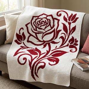 May include: A rectangular crochet blanket featuring a large, deep red rose motif centered on a white background. The design includes detailed petals, leaves, and swirling stems, all crafted with a consistent stitch pattern across the entire surface.