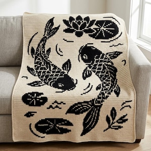 May include: A rectangular crochet blanket in cream with a black graphic pattern featuring two koi fish swimming in a circular motion, surrounded by lotus flowers, lily pads, and small aquatic plant motifs across the entire surface.