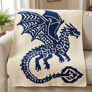 Può includere: Una coperta rettangolare all'uncinetto con una base color crema e un grande motivo a drago blu scuro centrato sul tessuto. Il drago è raffigurato di profilo con le ali spiegate, una lunga coda curva e intricati motivi geometrici.