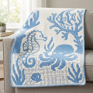 May include: A rectangular crochet blanket featuring a white background with a repeating blue pattern of marine life including a seahorse, an octopus, coral, and a seashell. The design is created with a grid-like stitch pattern throughout.