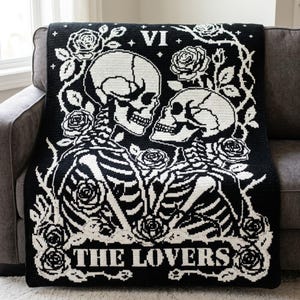 May include: A black and white crochet blanket featuring a graphic design of two skeletons facing each other, surrounded by roses and thorny vines. The top center displays the Roman numeral VI, and the bottom features the text THE LOVERS.