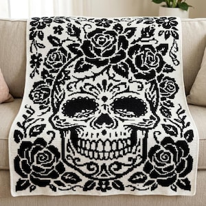 May include: A rectangular crochet blanket featuring a high-contrast black and white pattern. The design displays a large central human skull surrounded by intricate floral motifs, including detailed roses and leaves, covering the entire surface.