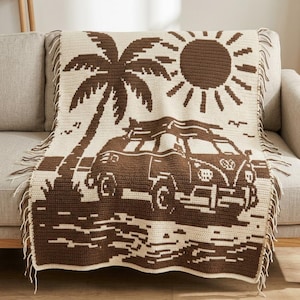 Könnte beinhalten: Eine rechteckige Häkeldecke mit einem zweifarbigen Design in Braun und Creme. Das Muster zeigt eine Palme, eine Sonne und einen Vintage-Bus an einem Strand. Die Decke ist an den beiden kürzeren vertikalen Kanten mit Fransen versehen.