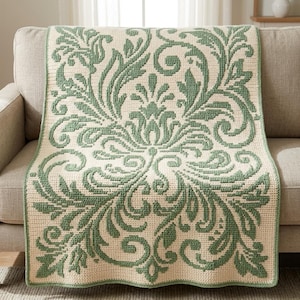 May include: A rectangular crochet blanket featuring a two-tone damask pattern in sage green and cream. The intricate design consists of symmetrical, swirling floral and leaf motifs that repeat across the entire surface of the textile piece.