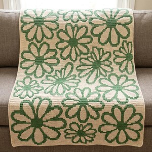 May include: A rectangular crochet blanket featuring a repeating pattern of large, stylized flowers. The design consists of dark green outlines and centers set against a cream-colored background, creating a high-contrast floral motif throughout.