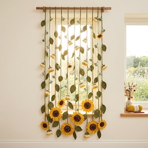 May include: A handcrafted crochet curtain featuring a sunflower design. The curtain has yellow sunflowers, green leaves, and stems hanging from a wooden rod. The curtain is displayed in front of a window, with sunlight shining through.