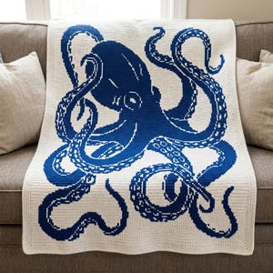 May include: A rectangular crochet blanket featuring a large, detailed blue octopus graphic centered on a cream-colored background. The octopus design is created with a pixelated or grid-like stitch pattern, showcasing its head and eight long tentacles.